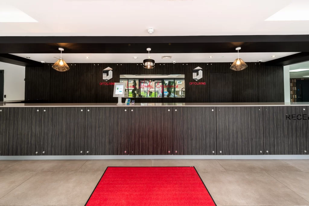 Entrance way to Opto Village with wide front desk and red carpet on the floor.