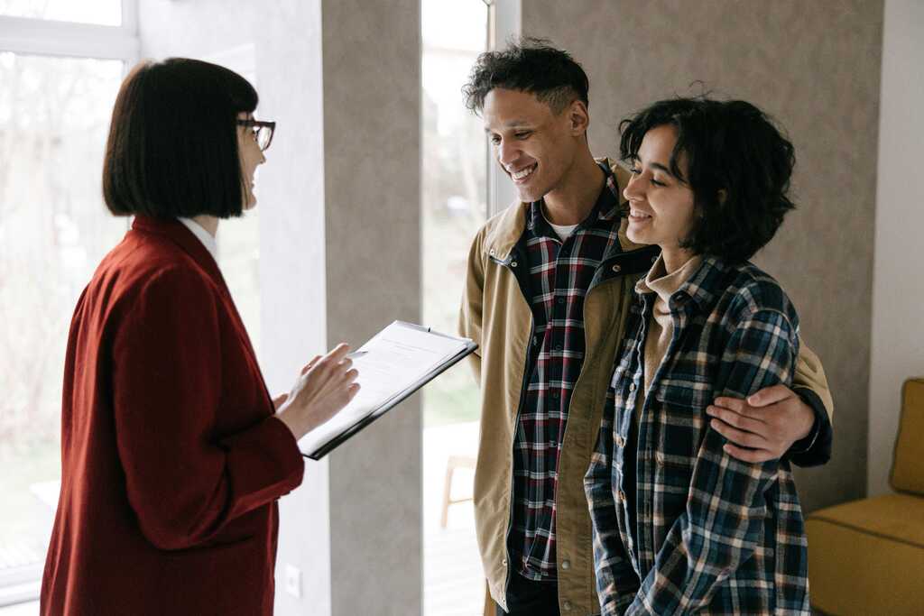 Woman with clip board, showing a man and woman around a home, who are hugging and looking happy