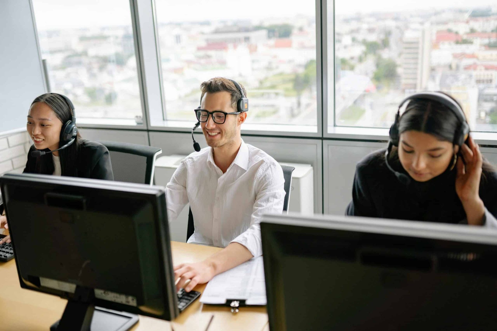 Two women an a man working on computers in an office with headsets on