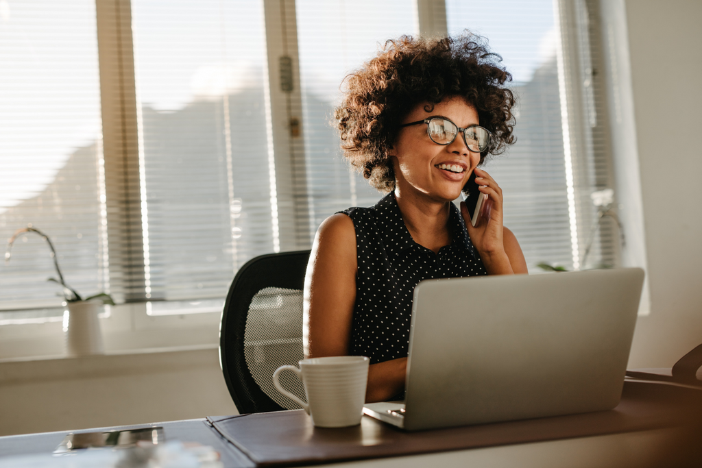 Woman in an office sat with her laptop speaking on the phone