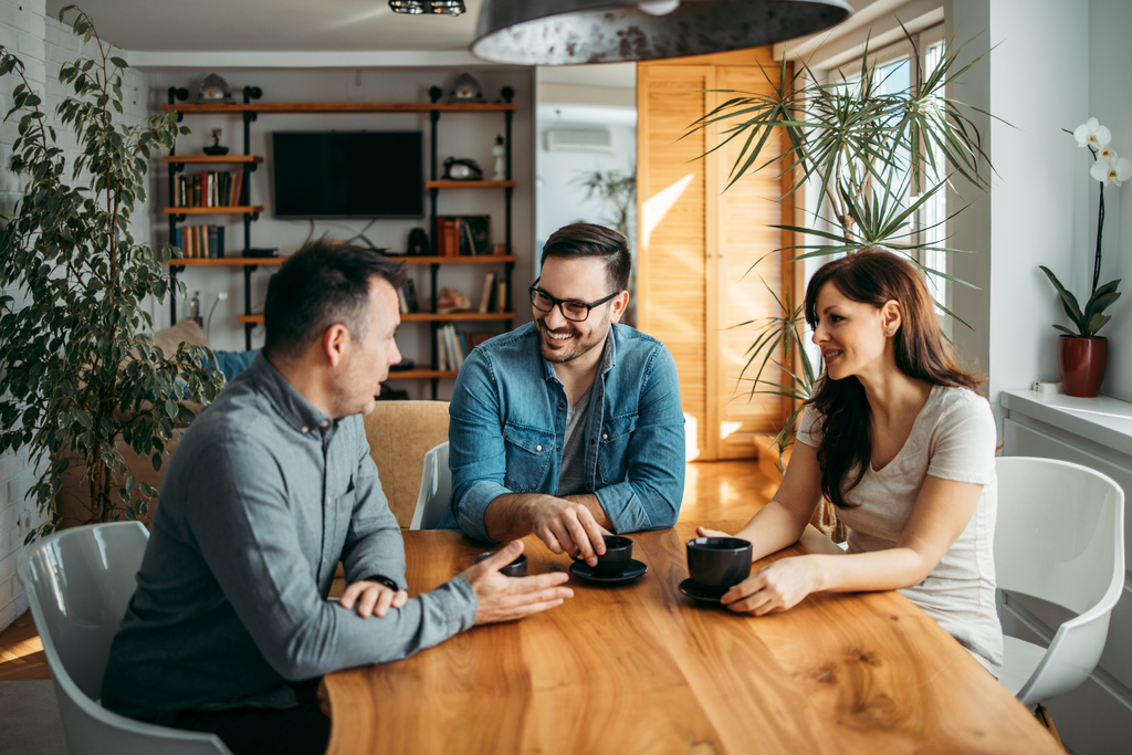 a woman and 2 men sat at a wooden table with a coffee talking with each other