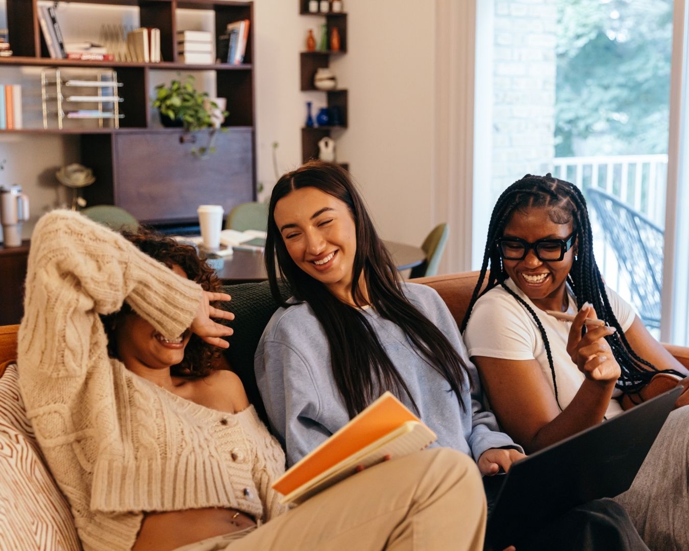 Three, female, University Students sat laughing on the sofa together